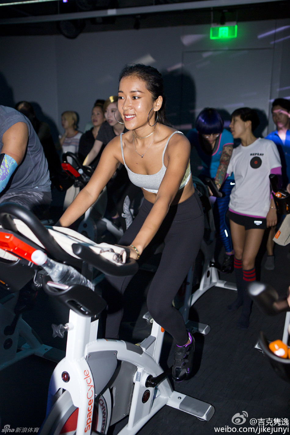 吉克隽逸与中国男篮队员们合影，她被高大的球员们簇拥在中间，脸上带着灿烂又有些俏皮的笑容，一身红色队服格外醒目，画面充满动感与和谐