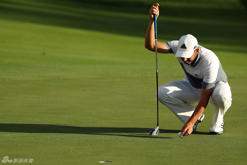 西班牙人正用一支球道木小心翼翼地推球，身体姿态略显别扭，凸显了在没有推杆时的无奈与挣扎。