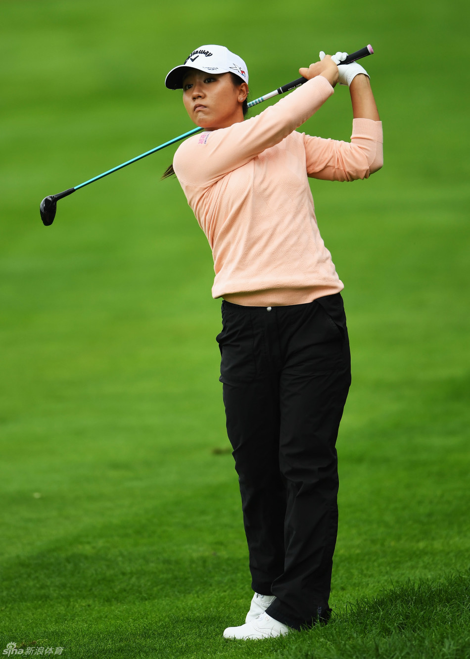 一位女子高尔夫球员脚踩一双闪耀夺目的金色高尔夫球鞋，正行走在球场上，时尚的装备成为赛场上一抹亮丽的色彩。