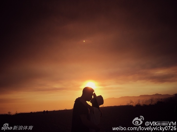 两人穿着印有卡通图案的白色情侣T恤，在充满生活气息的街角甜蜜牵手，李根低头看向妻子，眼神中满是宠溺与温柔。