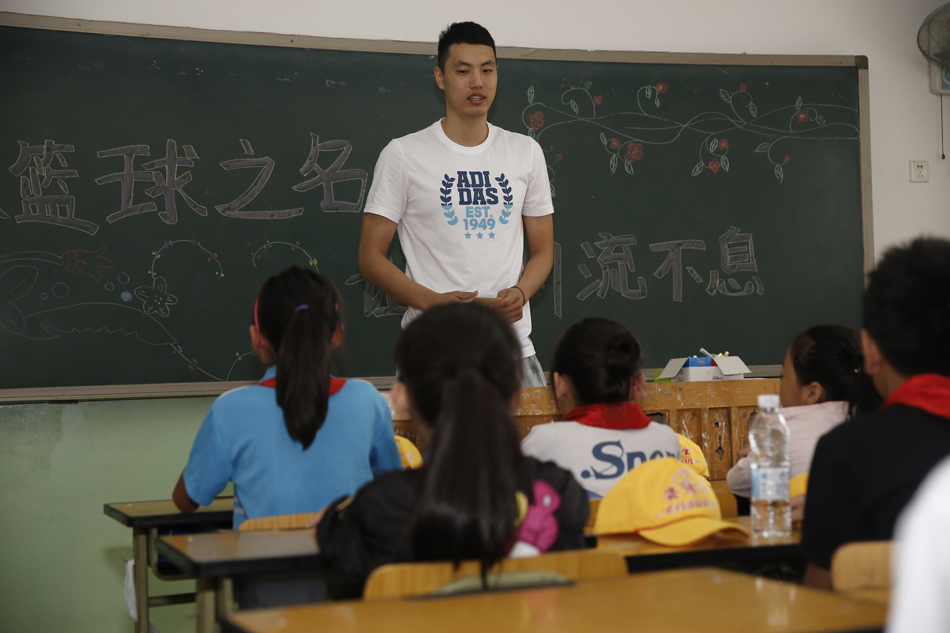 翟晓川在简陋的教室里与孩子们围坐在一起，他耐心地倾听一位小女孩说话，眼神温柔，孩子们紧紧靠在他身边，毫无距离感