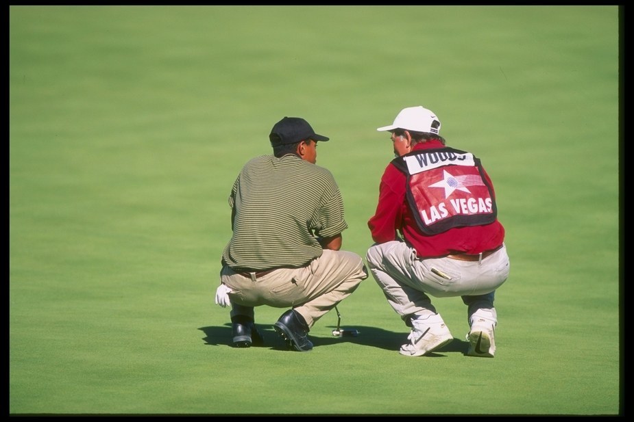 夺冠后，年轻的泰格·伍兹与他的球童‘Fluff’考文在果岭旁专注地研究推杆线路，两人的身影构成了信任与协作的经典画面。