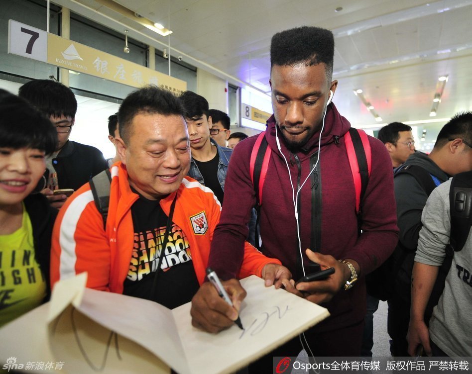 科尔俯身在一件山东男篮球衣上认真签下名字，旁边伸过来数只拿着纪念品的手，场面热烈而有序。