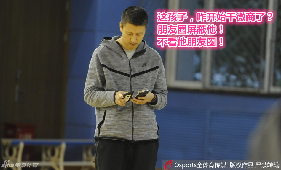 主帅郭士强手持手机却心系训练场，目光越过屏幕投向远处的弟子，面容沉静，眼神中透露出对球队备战情况的运筹帷幄。