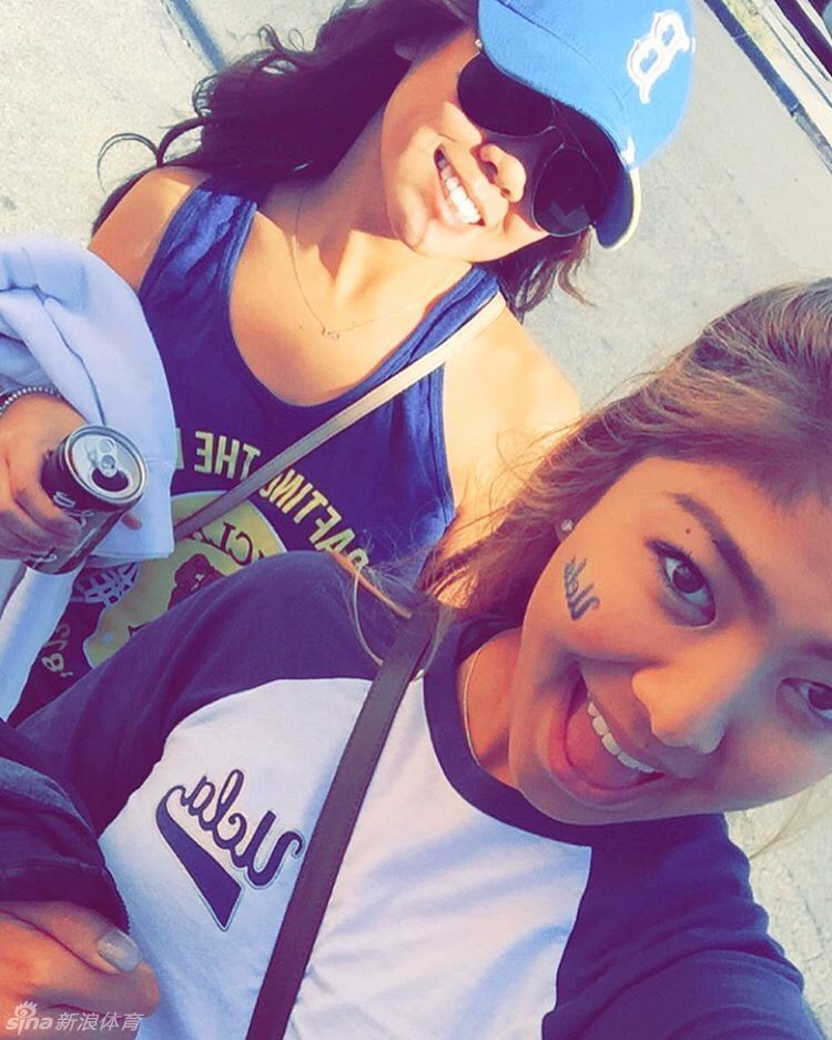 一名气质知性的女生在图书馆前回眸，眼神聪慧而沉静，身后是UCLA标志性的红砖建筑与蓝天。