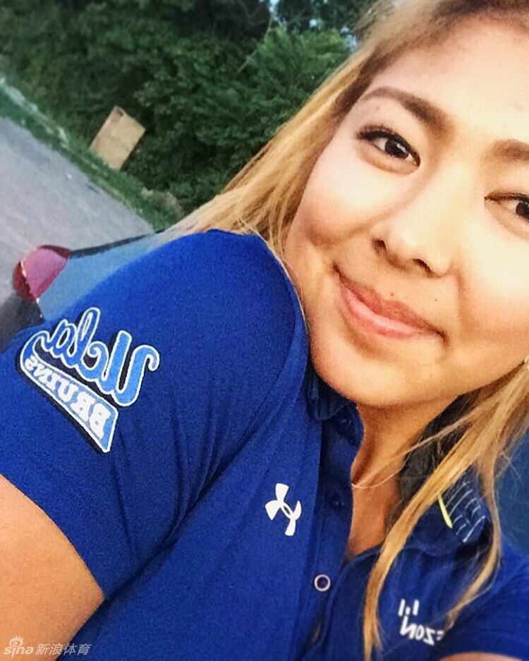 阳光灿烂的午后，一名小麦肤色、笑容灿烂的女生走在校园的露天台阶上，身后是郁郁葱葱的绿植和经典的校园建筑。