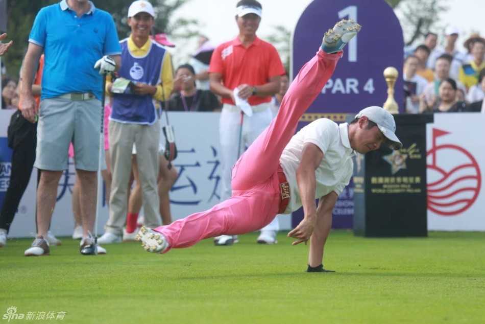 邢傲伟在观澜湖高尔夫球场发球台前自信站立，身穿醒目的修身粉红色长裤，与同组明星轻松谈笑，身后是广阔的绿茵球场与蓝天白云。