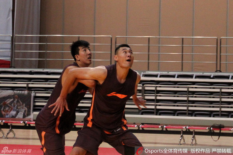 队医跪在地上，手法专业地为一名气喘吁吁的球员按摩小腿，球员脸上露出略显痛苦又放松的表情，身后的队友们还在进行投篮加练，动静之间尽显职业体育的严谨。