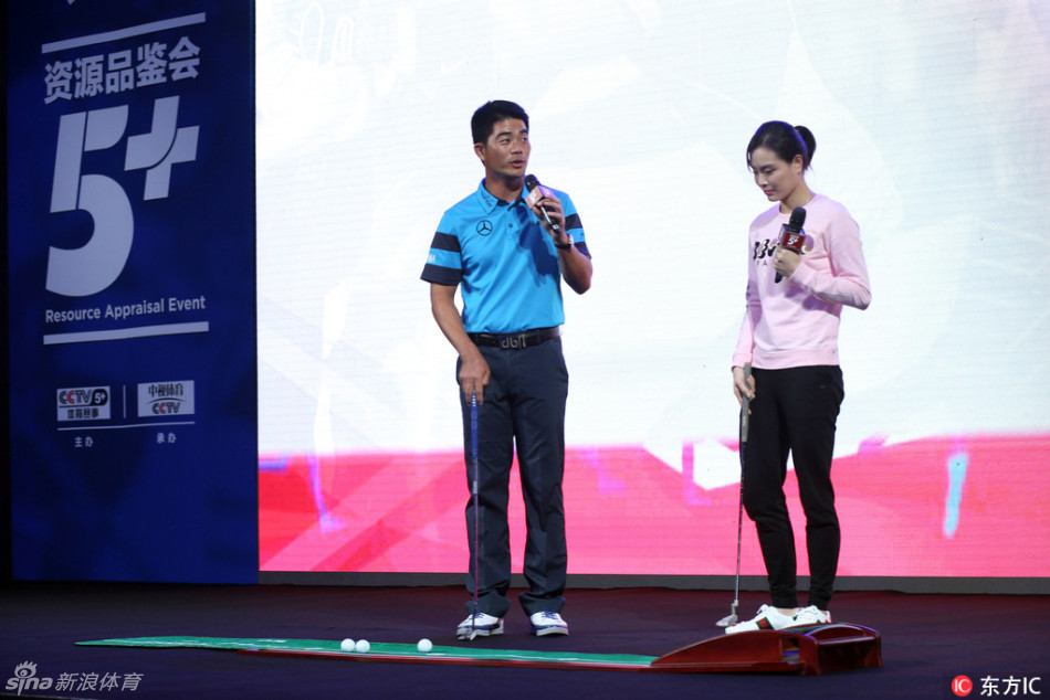 梁文冲手持推杆练习器,正向身旁的吴敏霞热情介绍,两人目光聚焦于器材,洋溢着对新体验的期待