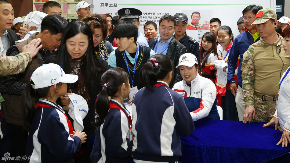 冯珊珊被层层热情的球迷包围，她正专注地在一顶帽子上签名，脸上洋溢着亲切的笑容