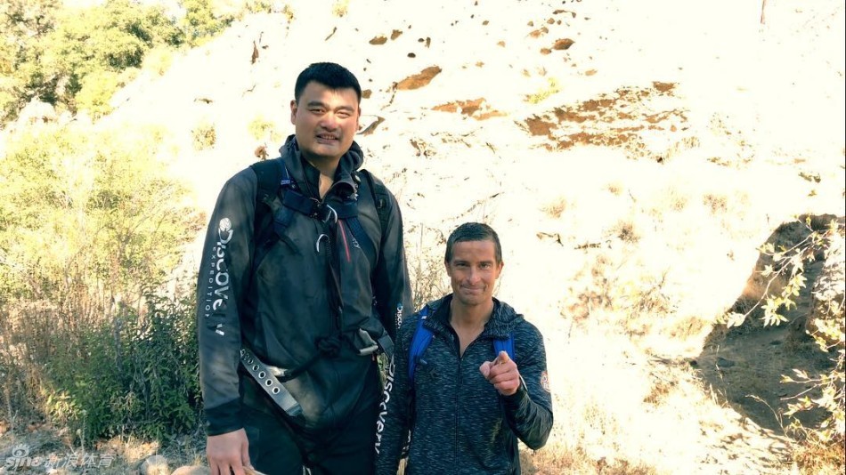 险峻的悬崖峭壁间，贝尔与姚明一前一后艰难穿行。巨大的身高差让画面显得既诙谐又惊险，在荒野面前，即便是篮球巨人，也必须小心翼翼地寻找每一个落脚点。