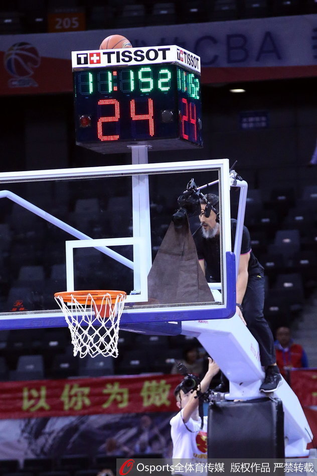 一名勇敢的工作人员爬上高高的篮球架，正伸出手臂去取卡在计时器上的篮球