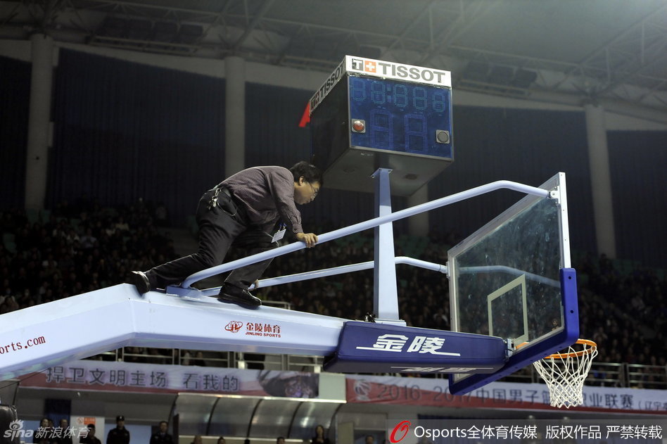 在漆黑的计时器下方，一名身穿工作服的技术人员站在梯子上，正仰头仔细检查着故障部件，而周围的灯光映照出他忙碌而无奈的身影。
