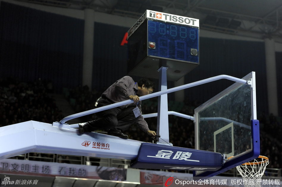 几名工作人员围聚在篮架后方，其中一人正在仔细地拨弄着计时器的线路，试图找出问题所在，场边的替补球员们也纷纷侧目关注着维修进展。