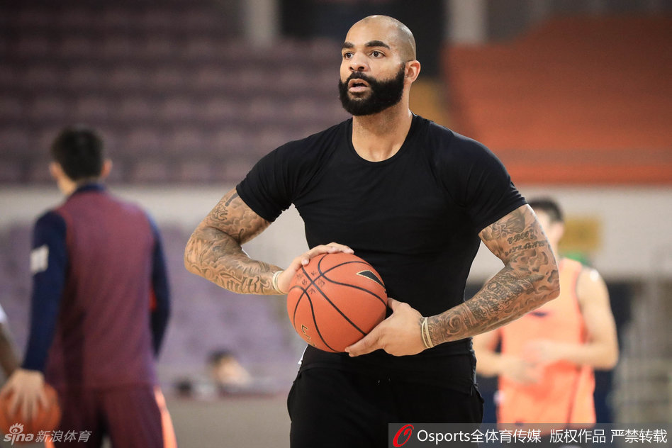 前NBA球星布泽尔神情专注，眉头微锁，在训练场上认真听取教练的战术布置，眼神中透露出不服输的坚韧。