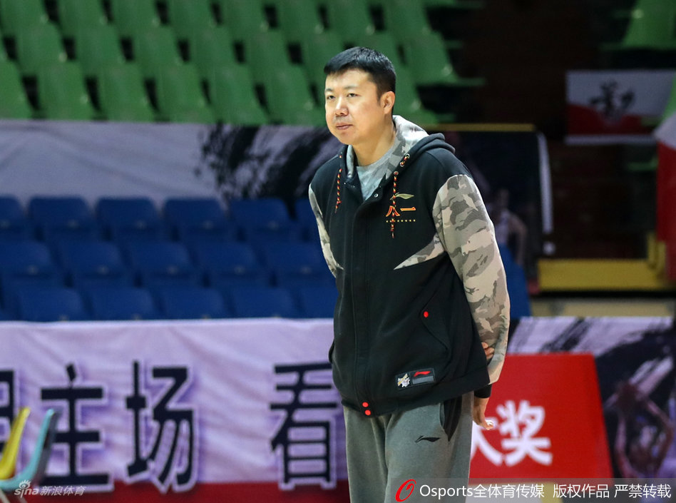 新任教练王治郅在场边神情专注地观看着队员们的训练，双臂环抱，眼神中透露出作为主帅的严肃与责任感。