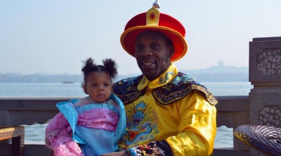 两个混血小宝贝穿着精致的中国风服装，大女儿抱着小女儿，在摄影师的镜头前摆出萌萌的姿势，眼神里充满对这个世界的好奇