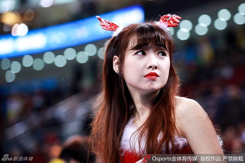 两位拉拉队员在场地边亲密互动，她们头上都戴着可爱的驯鹿角发饰，脸上洋溢着灿烂的笑容，圣诞气氛十足。