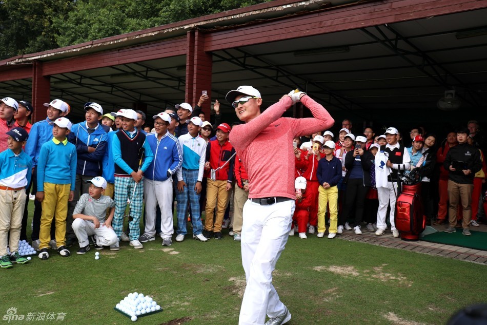 李昊桐在果岭边，身体微微前倾，正手把手指导一位小球员推杆的姿势与力度，画面温馨而专注。