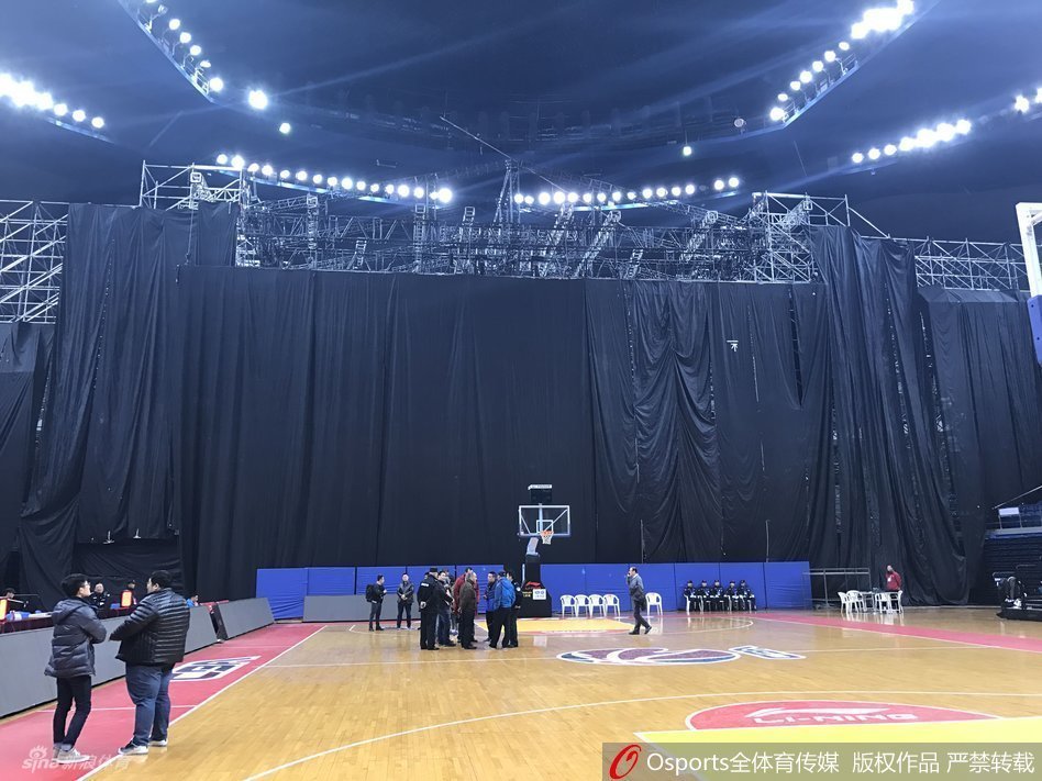 从高处俯瞰体育馆内场，演唱会舞台的规模几乎占据了半片看台区域，舞台边缘与篮球场的三分线距离极近，场边的广告牌显得微不足道，整个空间显得拥挤而错乱。