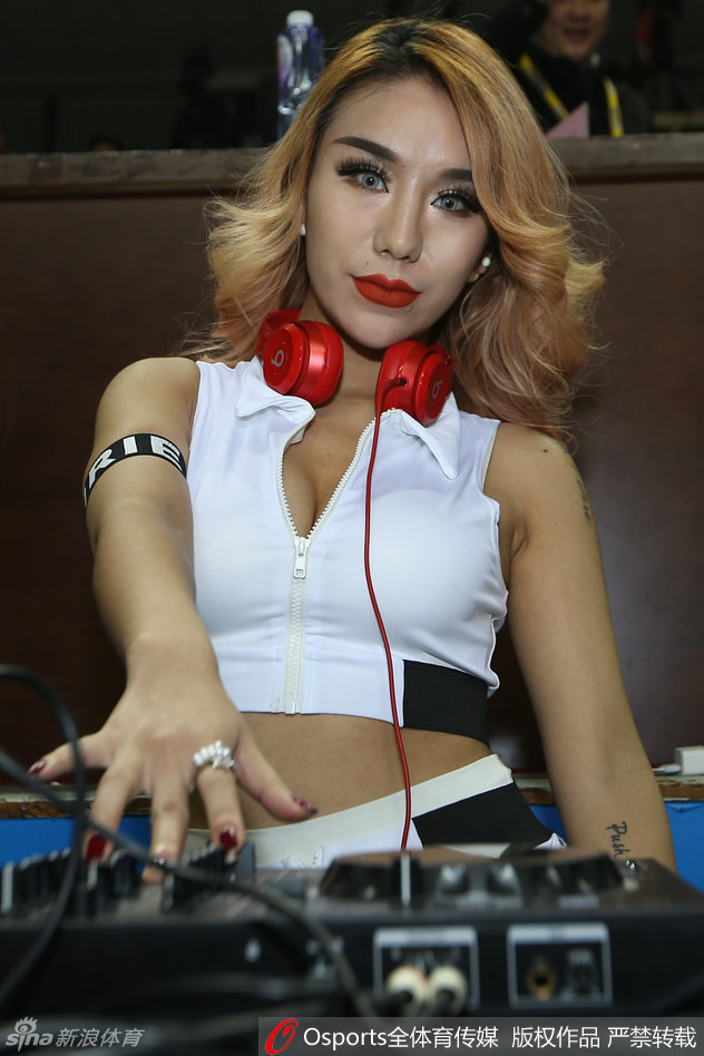 美女DJ在赛场边全神贯注地调试着混音台，精致的金发侧颜在灯光下格外迷人。