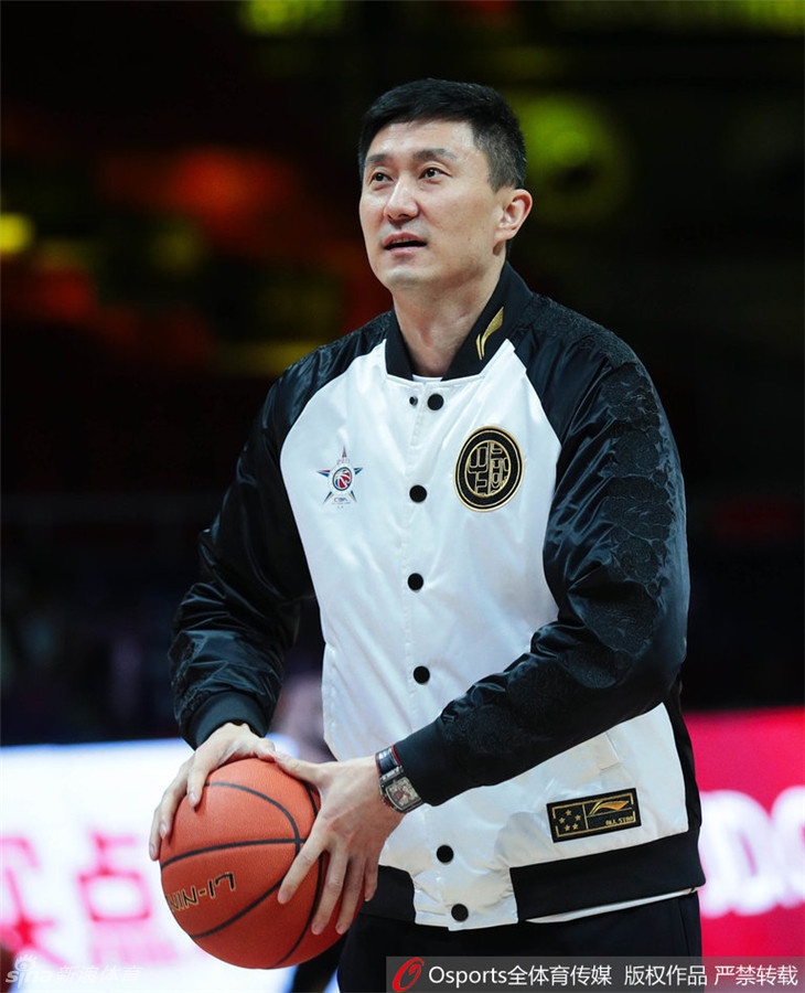 杜锋在场边接受媒体采访，手里拿着战术板，但目光不时看向一旁玩耍的儿子，神情专注而又夹杂着一丝作为父亲的牵挂。