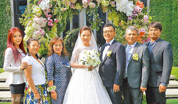 卢晓晴与新郎双方家人及亲友拍摄大合影,新人居中,众人笑容洋溢,背景是典雅的宴会大厅与喜庆的背景板