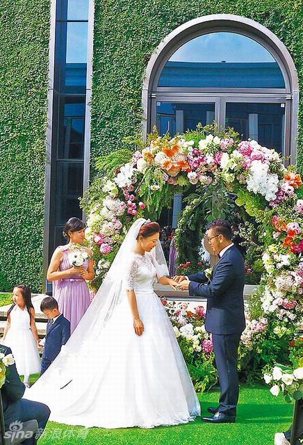 卢晓晴与新郎在装饰华丽的婚礼蛋糕前并肩而立,她手持香槟杯,正微笑着向全场宾客举杯致意