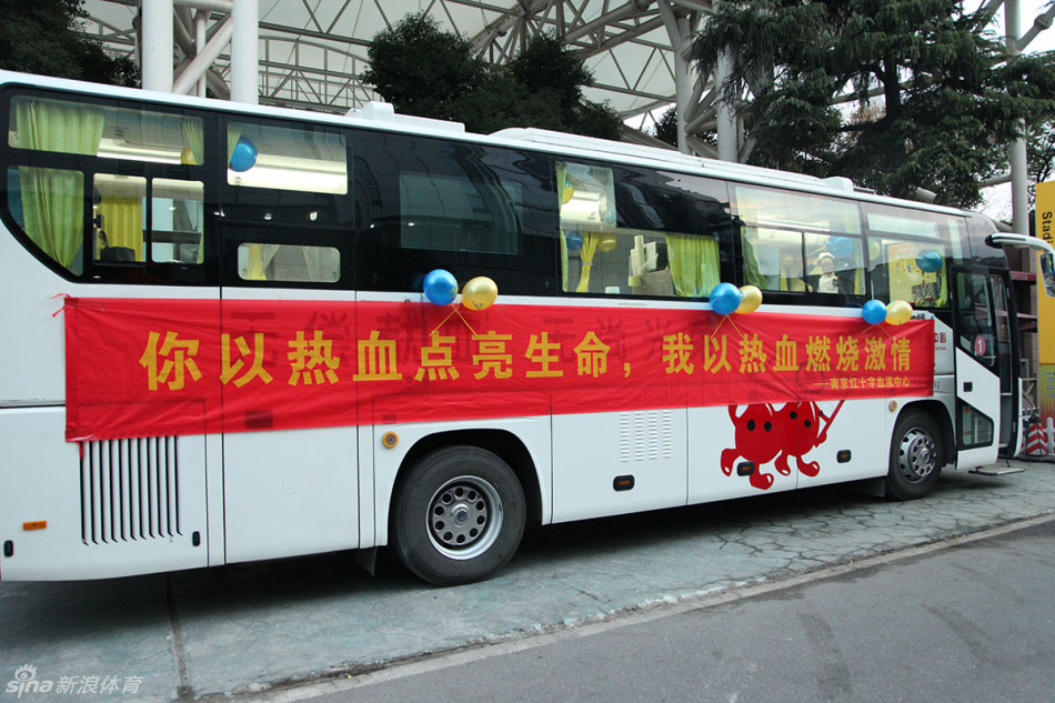 一辆喷绘着爱心标志的南京红十字血液中心献血车静静停靠在五台山体育馆外,车身标语在夜色中格外醒目,邀请过往球迷为生命加油。
