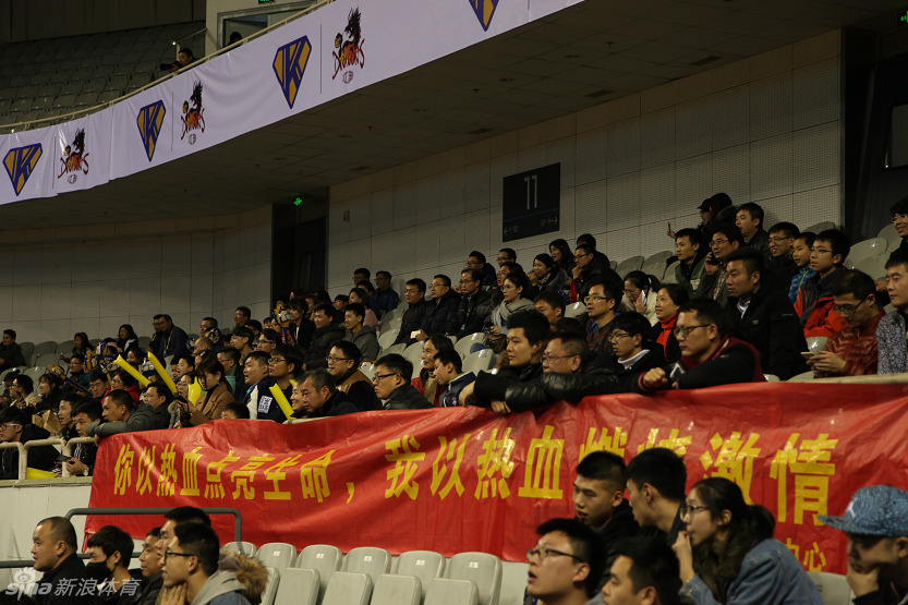 江苏肯帝亚队的主教练兼球员胡雪峰在场边接受媒体采访,他手持话筒,眼神坚定,身后是情绪高涨的球迷看台。