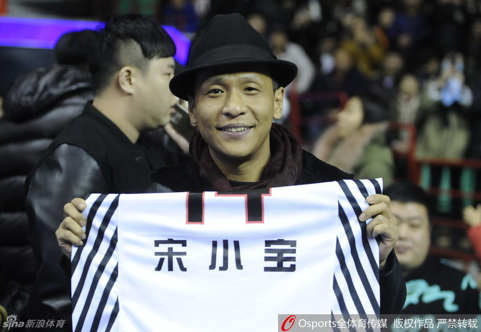 宋小宝双手高举哈德森赠送的14号特别版球衣，站在场边向全场球迷炫耀这份特殊的礼物，表情得意又搞笑，成为全场焦点。