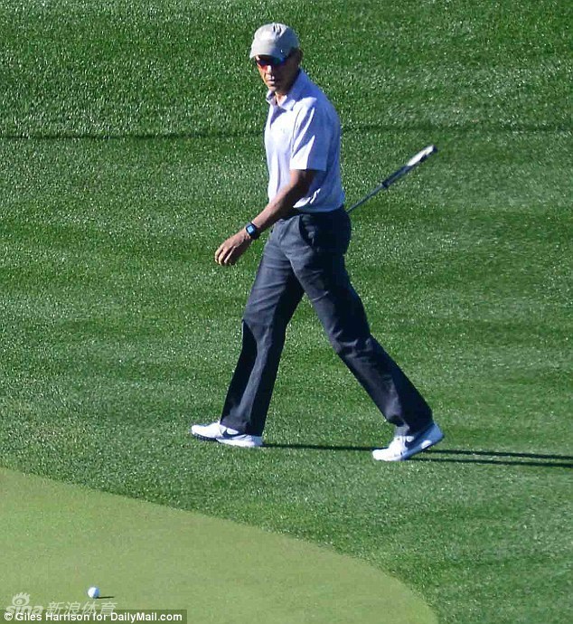 奥巴马在果岭上弯腰仔细观察球路，表情专注，身后是修剪整齐的草地与宁静的湖泊