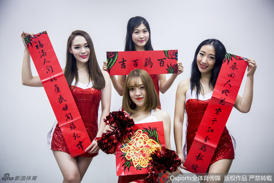 一名宝贝手持充满设计感的镂空扇子半遮面,眼神灵动俏皮,红色的新春装饰与球馆的蓝色座椅形成鲜明对比,洋溢着节日氛围