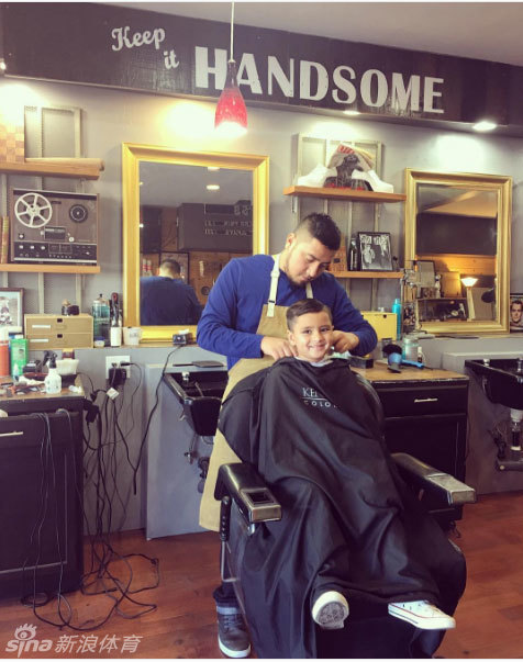 高尔夫名将贾森·戴伊俯身，温柔地为坐在理发椅上的儿子系上围布，眼神中满是父爱