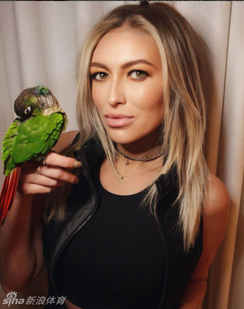 宝琳娜·格雷茨基怀抱色彩斑斓的鹦鹉展露笑颜，人与动物自然和谐的景象充满活力与趣味