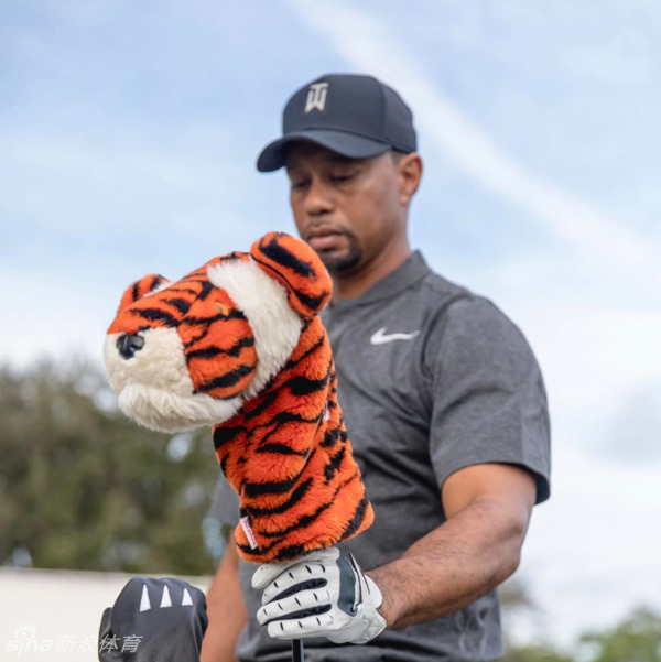 老虎伍兹手持新款高尔夫球具面对镜头露出神秘微笑，仿佛在预告一个即将到来的重磅消息