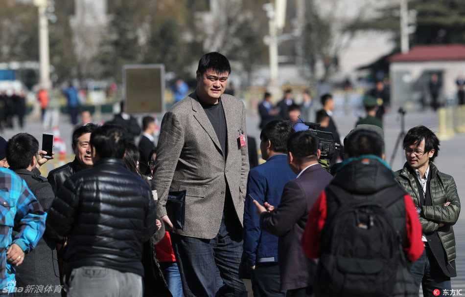 姚明现身NFL超级碗现场，他身着深色西装坐在看台上，周围是山呼海啸的球迷，他则神情专注地关注着场上的逆转大戏。