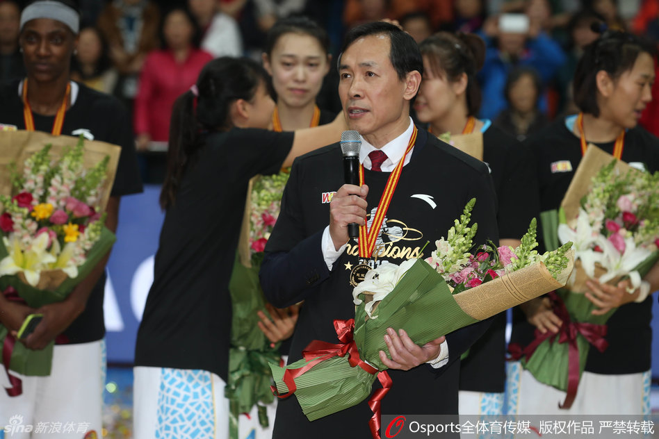 北京女篮全体成员在夺冠后于场地中央拍摄全家福,队员们有的抱着花束,有的高举着象征荣誉的手指,每个人的脸上都洋溢着幸福满足的微笑。