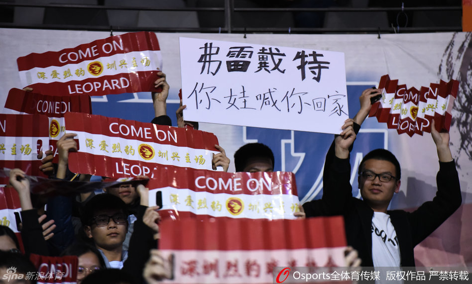 比赛进入白热化阶段，全场球迷起立，一位戴着眼镜的斯文球迷也忍不住振臂高呼，他手中挥舞的围巾上写着‘深圳’，将个人情感与城市荣耀紧密相连。