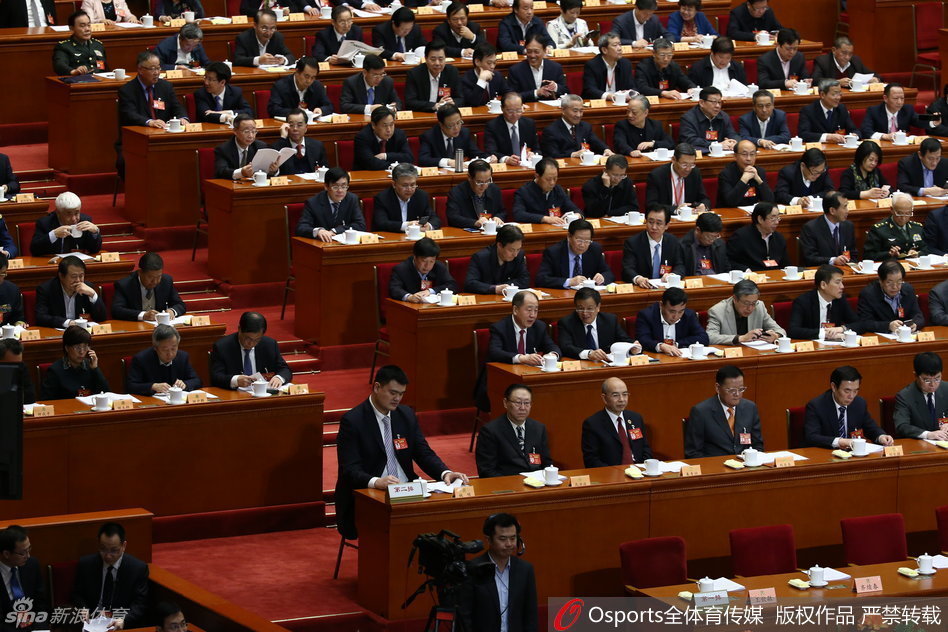 在座无虚席的万人礼堂中，姚明微微侧身，专注地与身旁的委员交换看法，他高出座位一截的身影在人群中极为醒目，周围委员或侧耳倾听或点头示意，氛围专注而融洽。