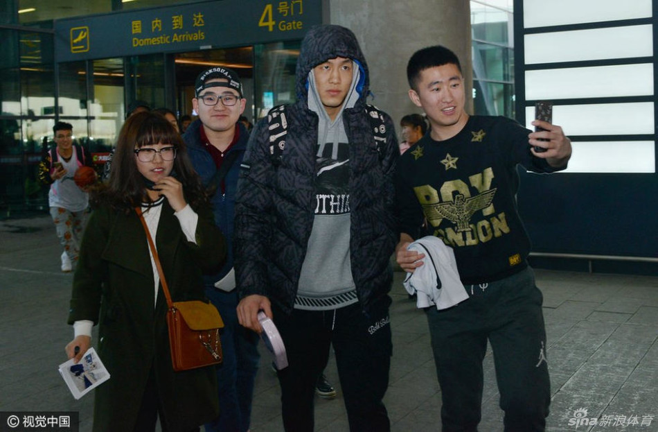 身穿黑色长款羽绒服的郭艾伦神态亲和,微微弯腰俯身,正在为一位身着蓝色辽篮球衣的小球迷认真地签名,周围是无数高举手机记录这一刻的热情人群。