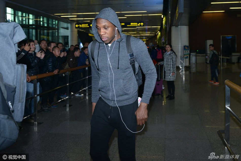 哈德森戴着黑色毛线帽和红色耳机,身背双肩包,双手插兜,面无表情地低头匆匆穿过人群,仿佛将自己封闭在独立的世界里,隔绝了周围的嘈杂。