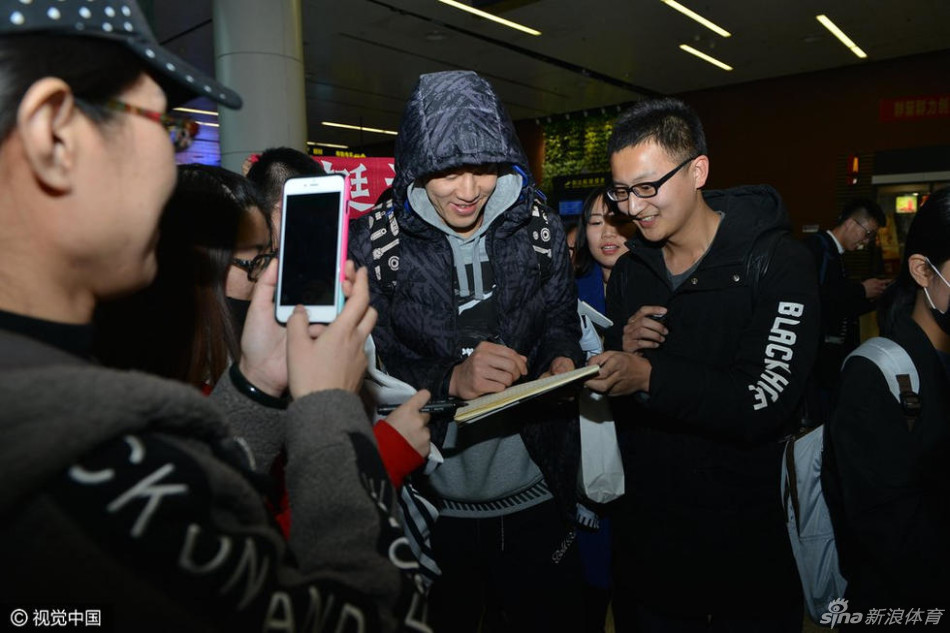 郭艾伦在人群中停下脚步,手持黑色马克笔,正专注地在一位女球迷递来的球衣上留下签名,侧脸轮廓在嘈杂的人群中显得格外认真与暖心。