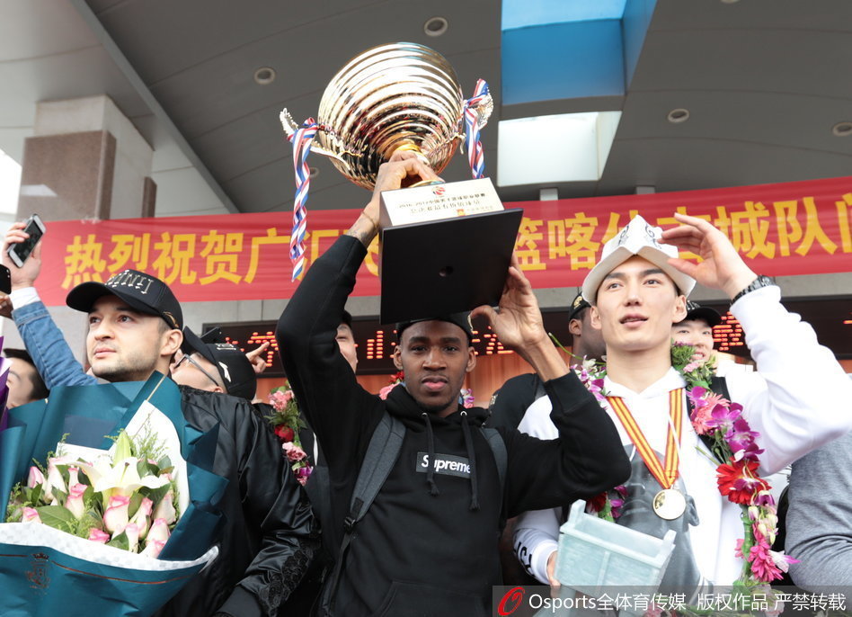 新疆男篮全体成员在球队专机前合影留念，总冠军至尊鼎在阳光下熠熠生辉，每个人的脸上都绽放着胜利的笑容，记录下这属于新疆篮球的历史性时刻。