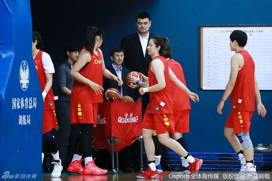 篮协主席姚明身着深色西装，神情专注地站立在场边，手中把玩着篮球，目光却始终追随着场上挥汗如雨的姑娘们，仿佛在思索中国女篮的未来之路。