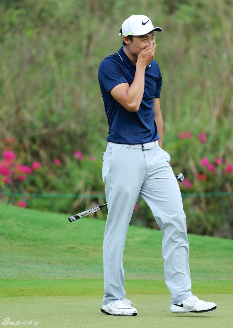 梁定丰在比赛中稳健挥杆，身体扭转充满张力，背景中的绿茵赛场广阔而宁静。