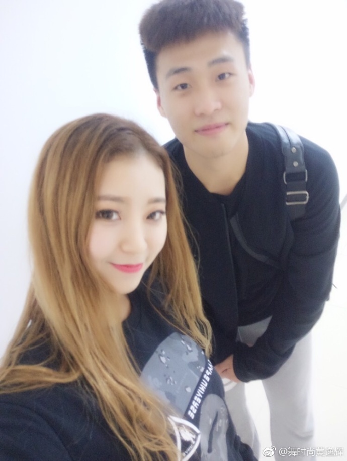 黄逸辉被几位宏远队的小鲜肉环绕在中间,她开心地对着镜头比心,身后是球员们略带青涩的笑容,画面充满活力。