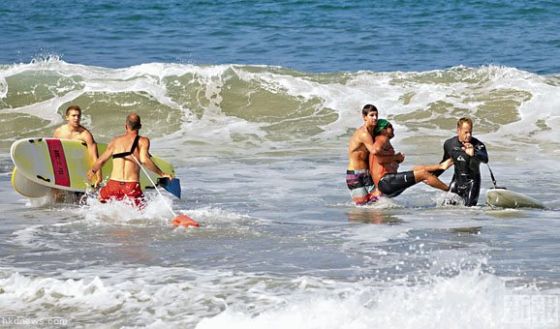 滑浪人士合力将被大白鲨咬伤男子抬上岸，男子的腰间仍有血流着。