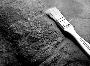 工作人员用小刷子、小凿子在一块巨大的墨绿色石块上东扫西敲