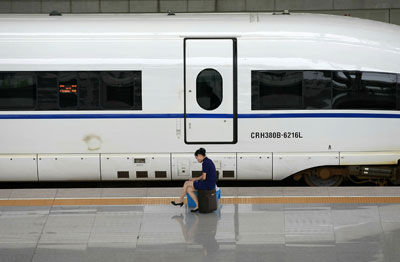 　　2011年7月12日，上海虹桥站站台上，一位高铁列车员坐在自己的行李箱上。她面前是已经晚点45分钟还没发车的G156次列车。